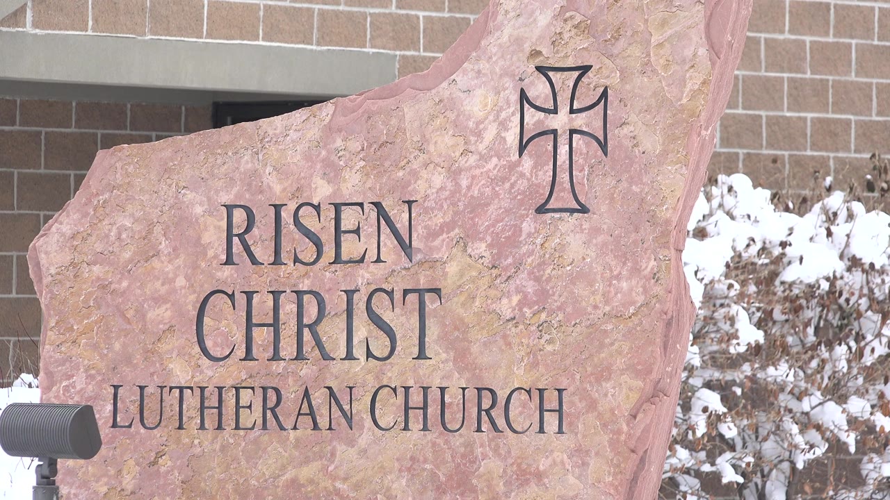 Stone Risen Christ Lutheran Church sign beside a brick building and snowy shrubs.