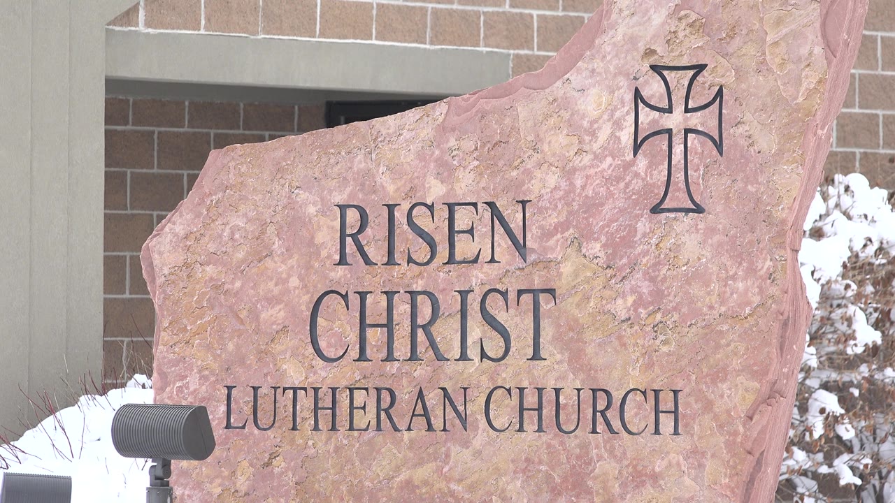The sign remains centered in Arvada, Colorado, with the engraved Risen Christ Lutheran Church lettering, a cross mark near the top, and no visible people.