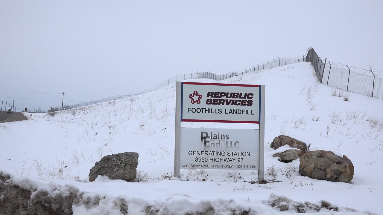 Snowy roadside landfill sign below a fenced ridge