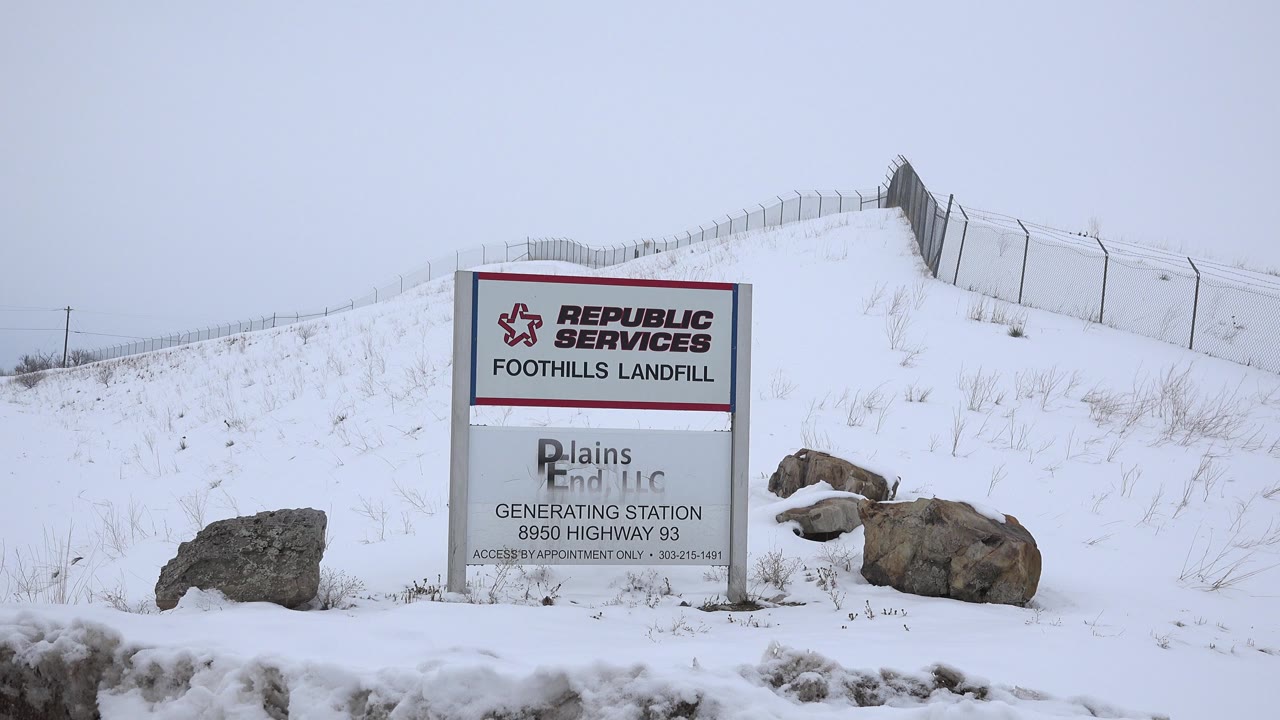 Landfill entrance sign on a snowy hillside with rocks nearby.