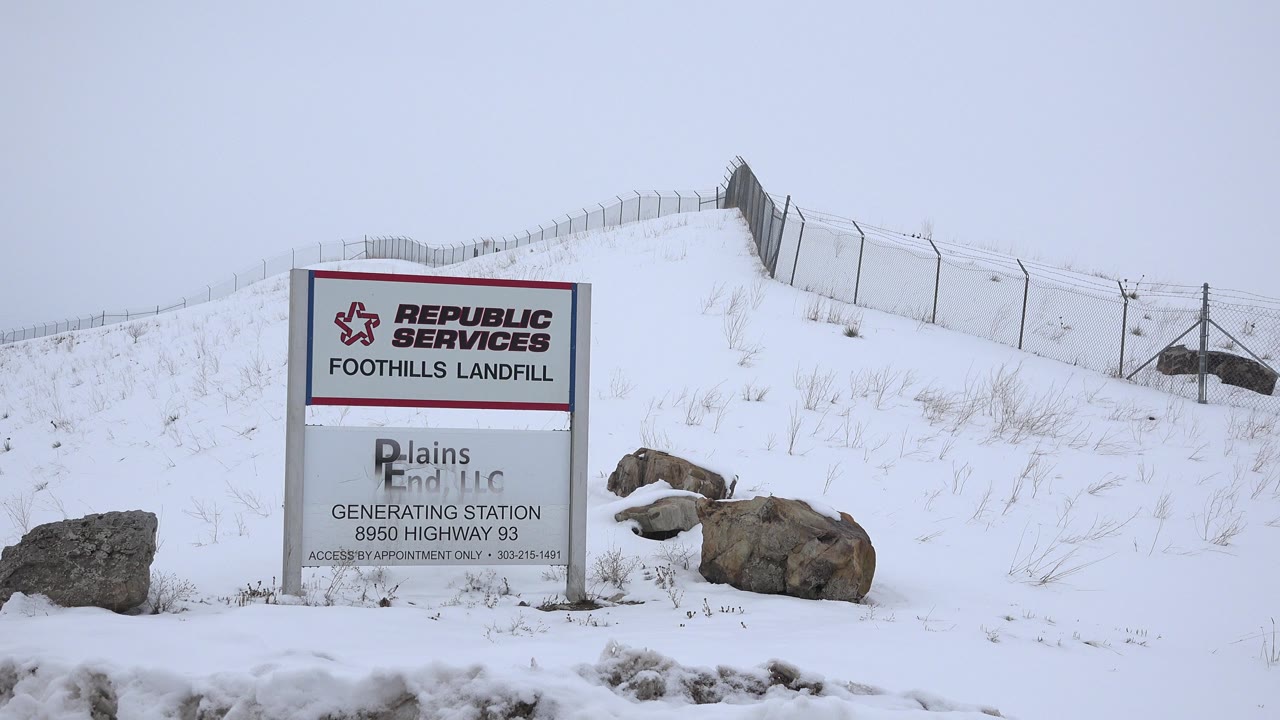 A second view of the Arvada landfill sign holds the sign near the left side of frame, with snow-covered rocks beside it and no visible people.