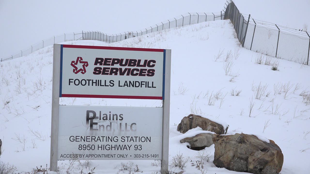 Landfill sign beside snowy rocks and fenced hill