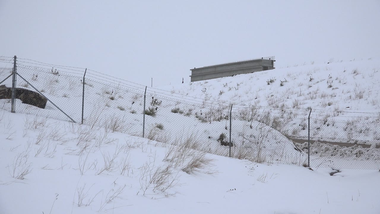 Fenced snowy slope with a road barrier at the top.