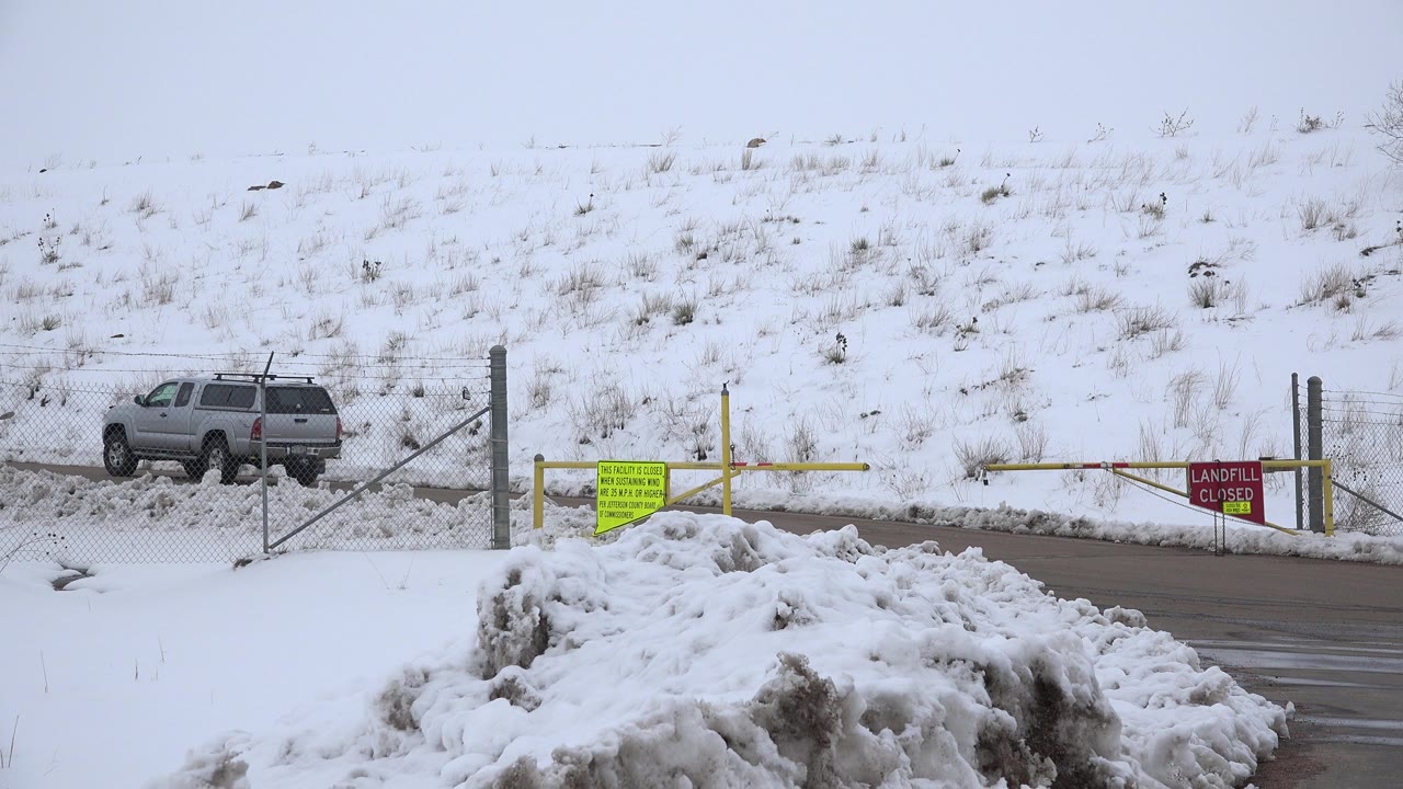 The gray SUV remains near the left side of the gated snowy entrance in Arvada, Colorado, with yellow barrier arms, a red closed sign, and no visible people.