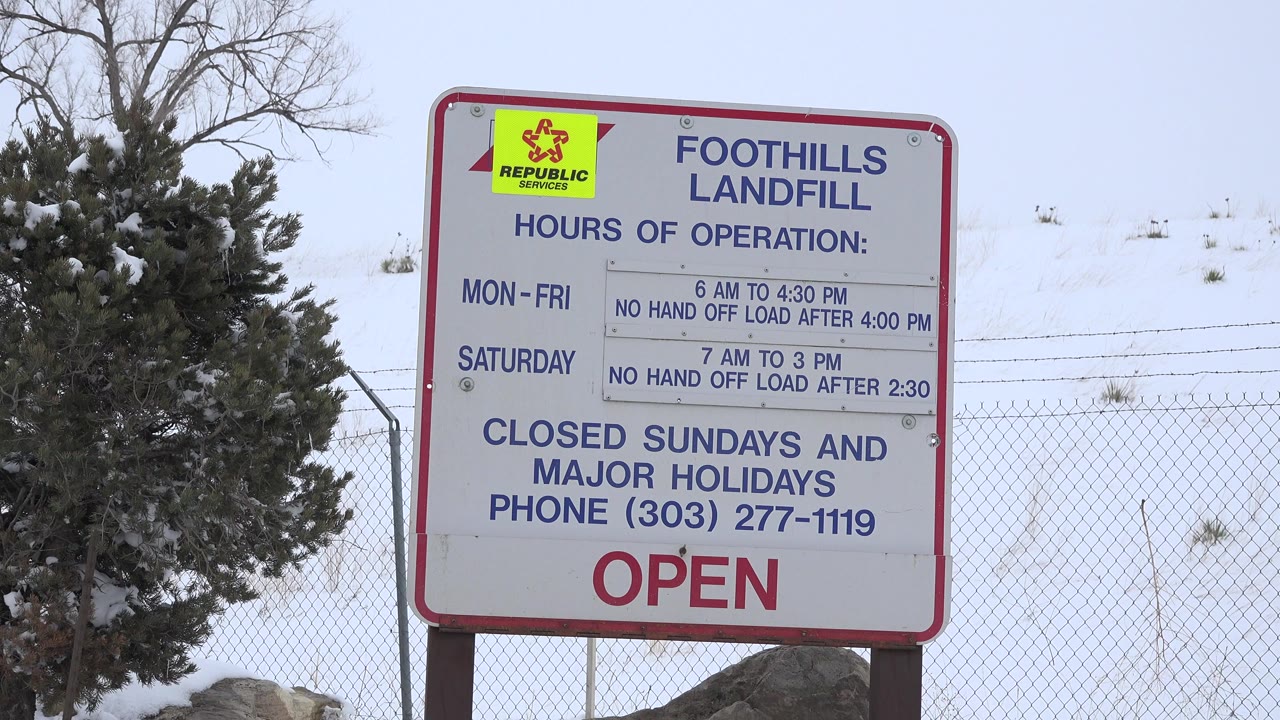 Foothills Landfill hours sign in Arvada, Colorado with a Republic Services logo, snowy trees, chain-link fence, pale sky, and no visible people.