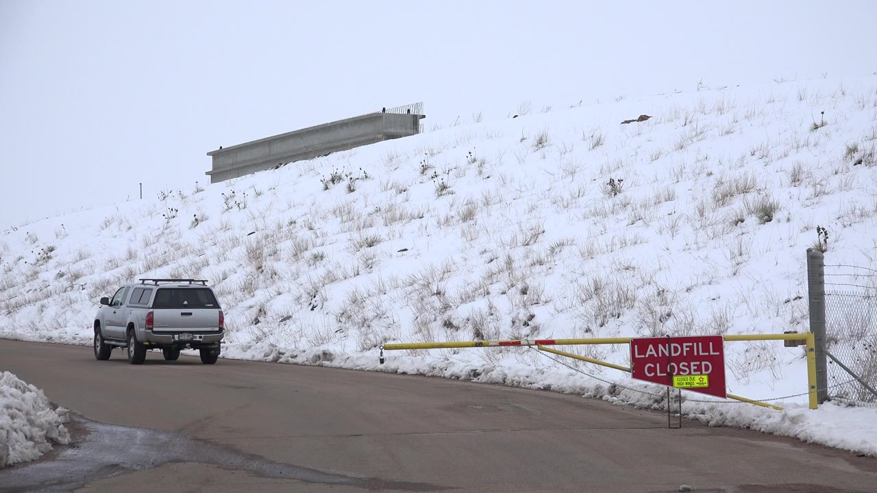Silver SUV beside a closed landfill gate on a snowy road.