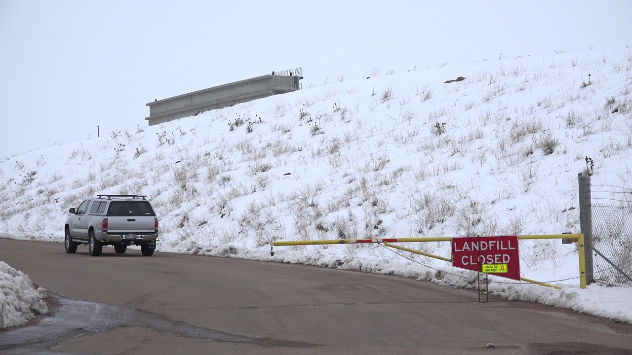Silver SUV on a snowy road beside a closed landfill gate.