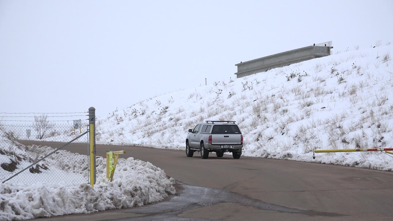 One second in, the silver SUV remains near the gated road entrance in Arvada, Colorado, with yellow posts, chain-link fencing, piled snow, and no visible people.