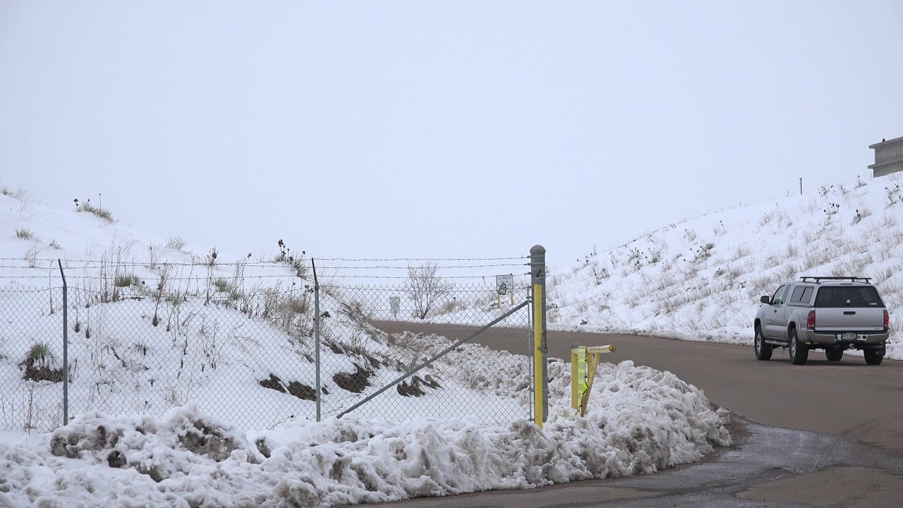 Grey SUV on a snowy roadside beside a chain-link fence