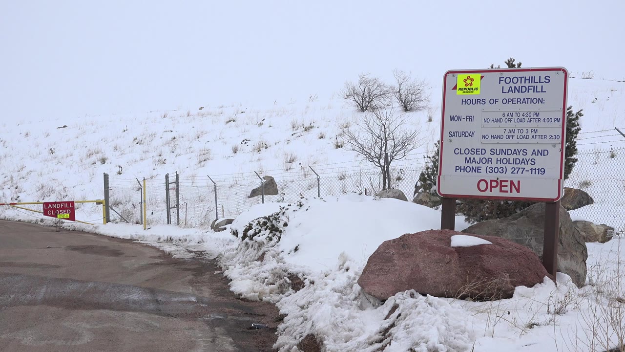 Snowy roadside with Foothills Landfill sign and rocks.