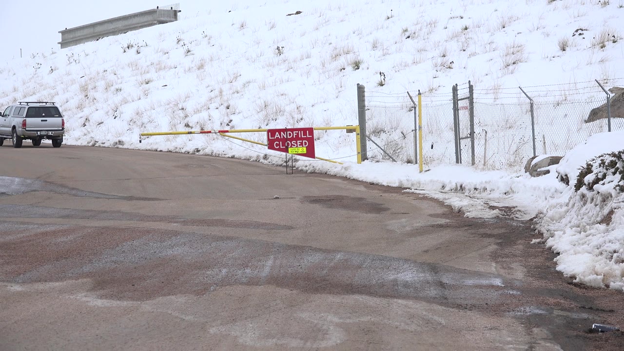 Silver SUV near a snowy gated road entrance with a landfill closed sign.