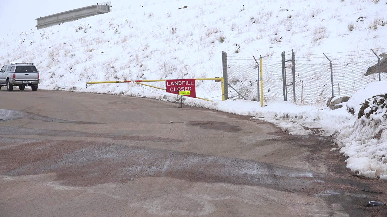 One second in, the vehicle is farther toward the left edge as the snowy Arvada road, yellow barrier arm, fence posts, and red landfill closed sign remain central, with no visible people.