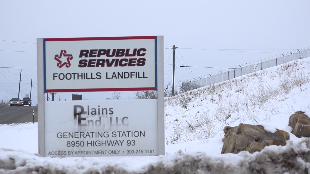 Roadside landfill and generating station sign beside a snowy hill.