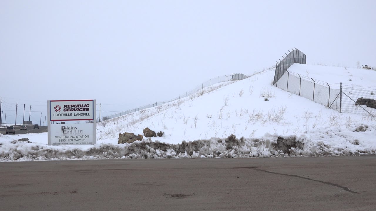 Snow-covered landfill entrance beside a paved road