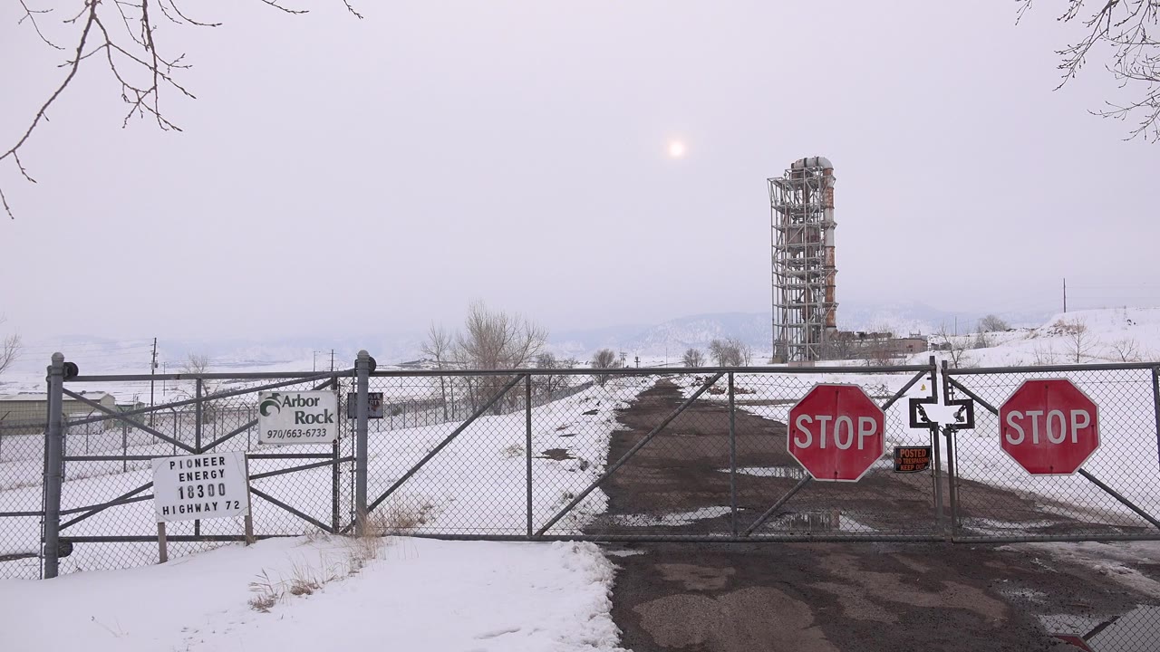 Snowy gated road with stop signs and a scaffolded tower beyond the fence