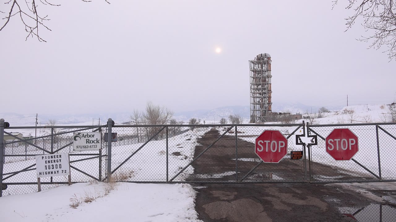 Snowy road blocked by a chain-link gate with red stop signs.