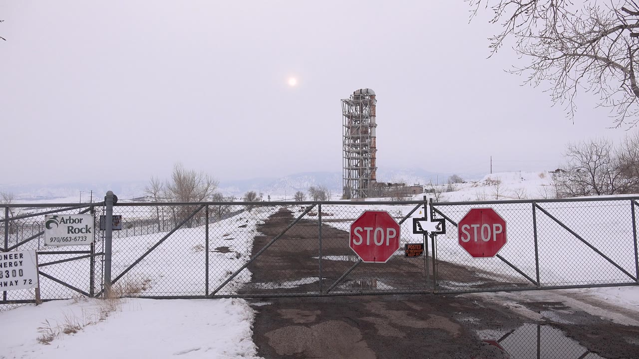 Snowy road blocked by chain-link gate with stop signs