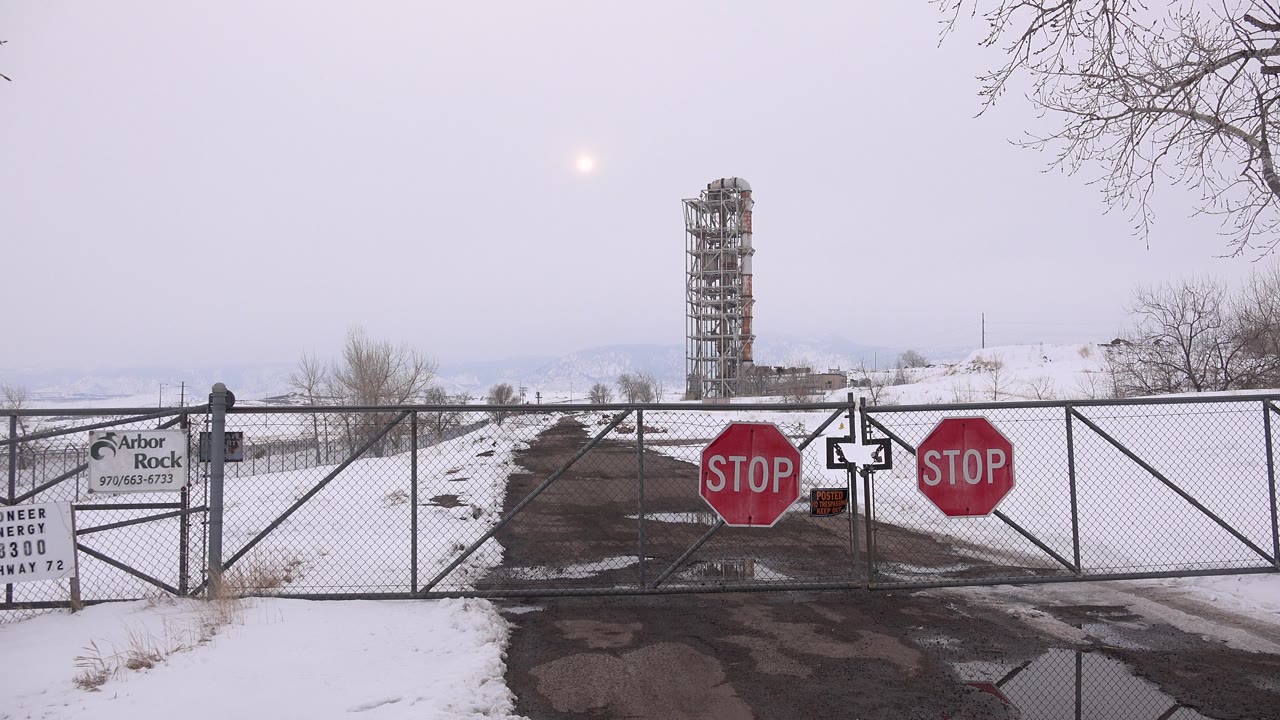The closed Arvada road is framed with the gate across the center, stop signs on both gate panels, snowbanks beside the pavement, and no visible people.