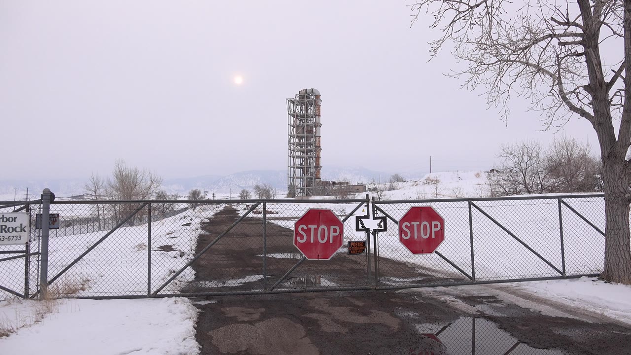 Arvada, Colorado frame with the gated road centered, stop signs on both sides of the gate, snowbanks along the pavement, a bare tree at right, and no visible people.