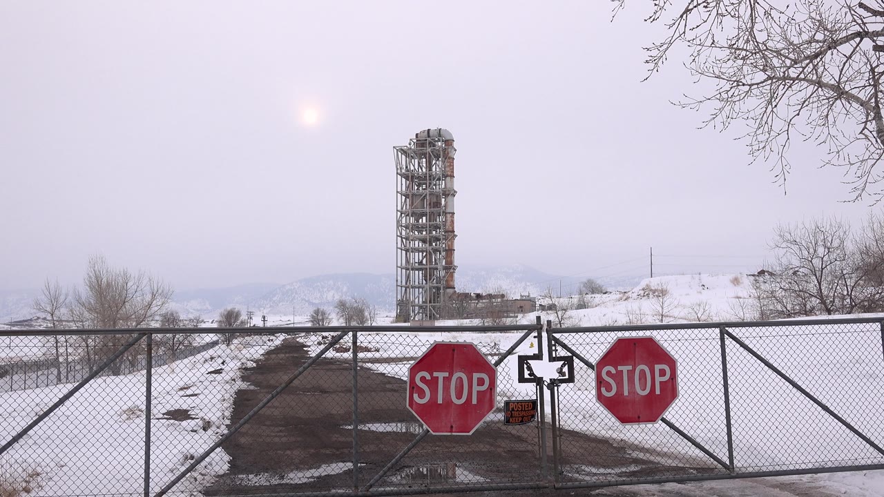 Closed chain-link gate with red stop signs beneath a pale cloudy sky.