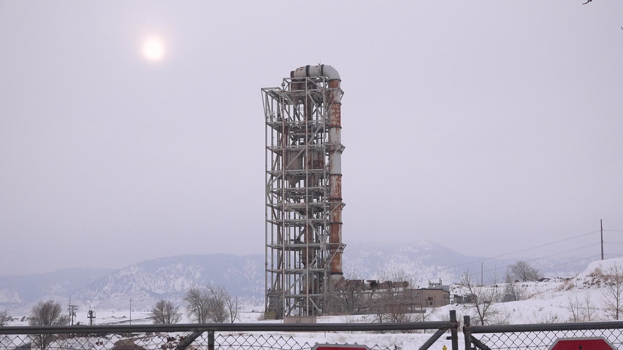 A steel construction tower rises above snow in Arvada, Colorado, with a pale sun high in the sky and no visible people.