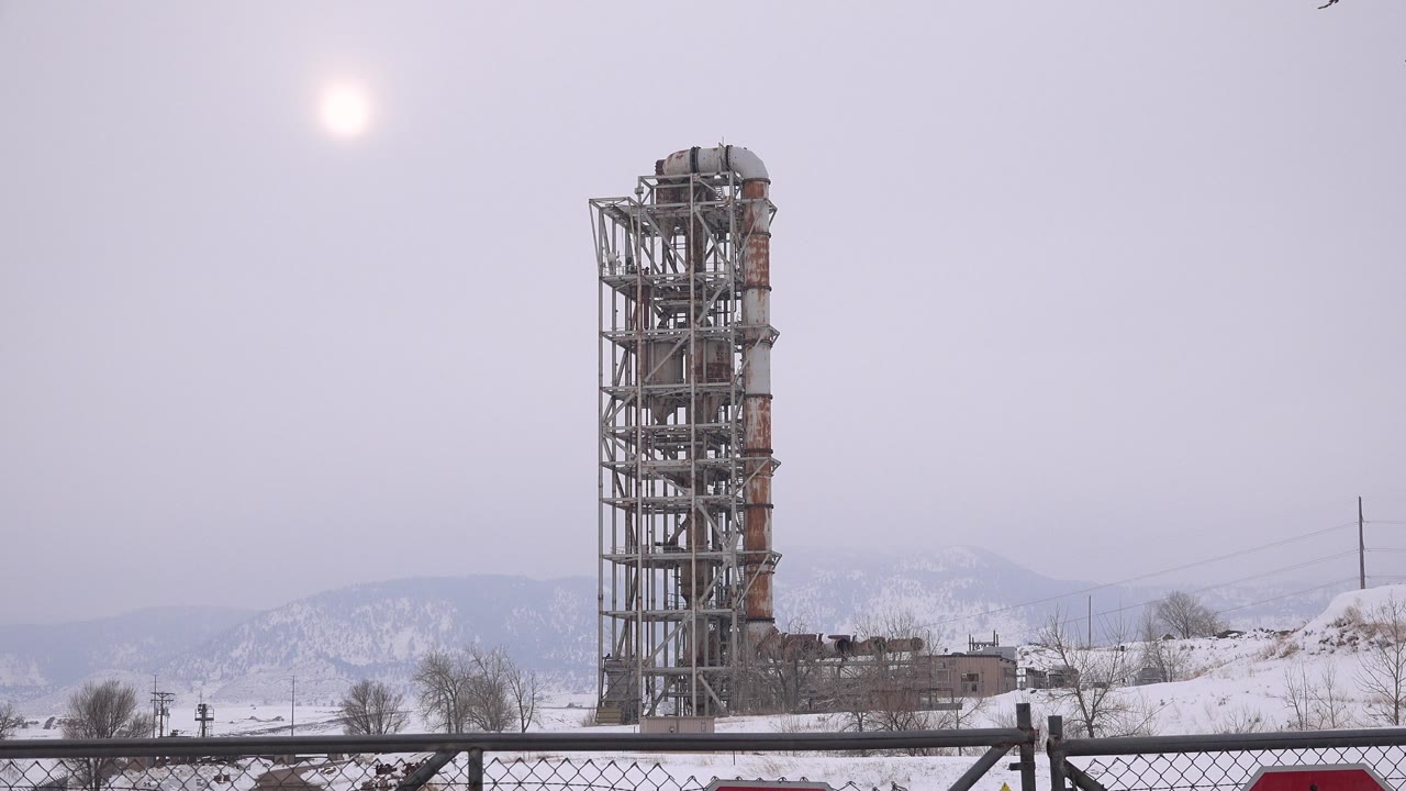 The tower remains centered in Arvada, Colorado, with the bright winter sun above, snowy ground below, and no visible people.