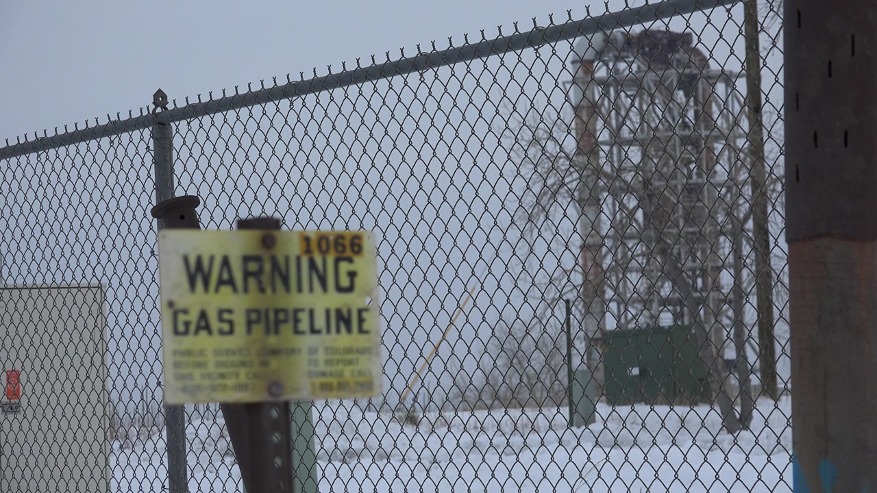 Warning gas pipeline sign near a chain-link fence and snowy utility yard.