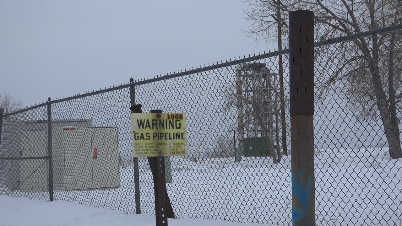 Snowy fenced utility site with gas pipeline warning sign