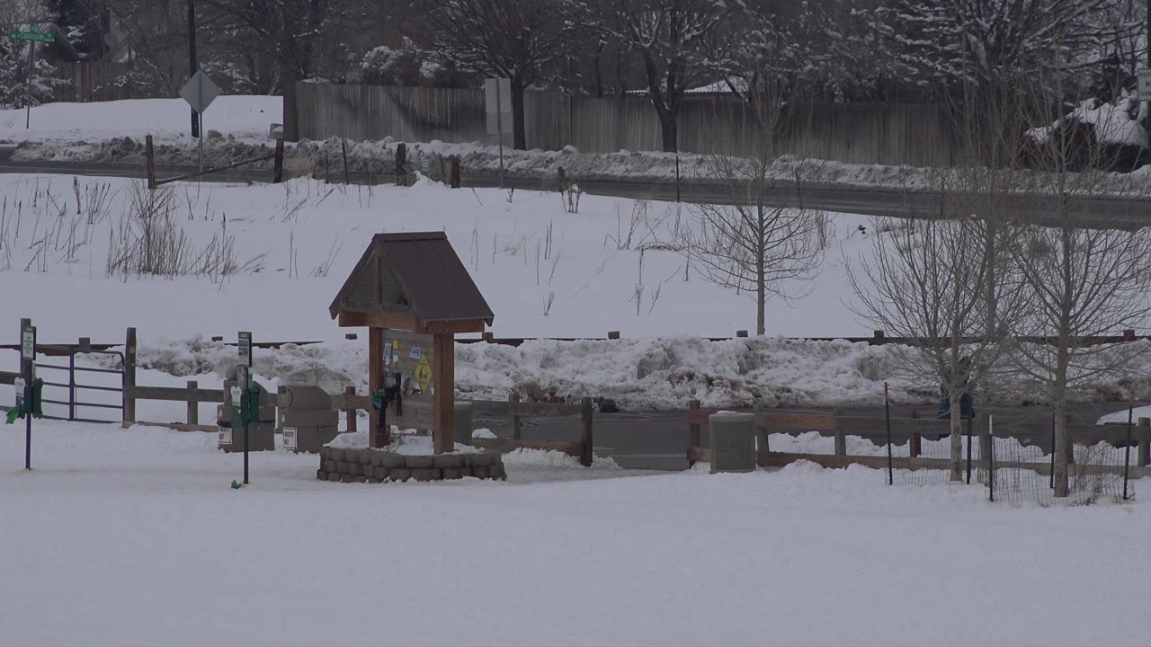 The Arvada park view holds on the wooden kiosk and fence, with snowbanks along the road and leafless trees in the gray winter background.