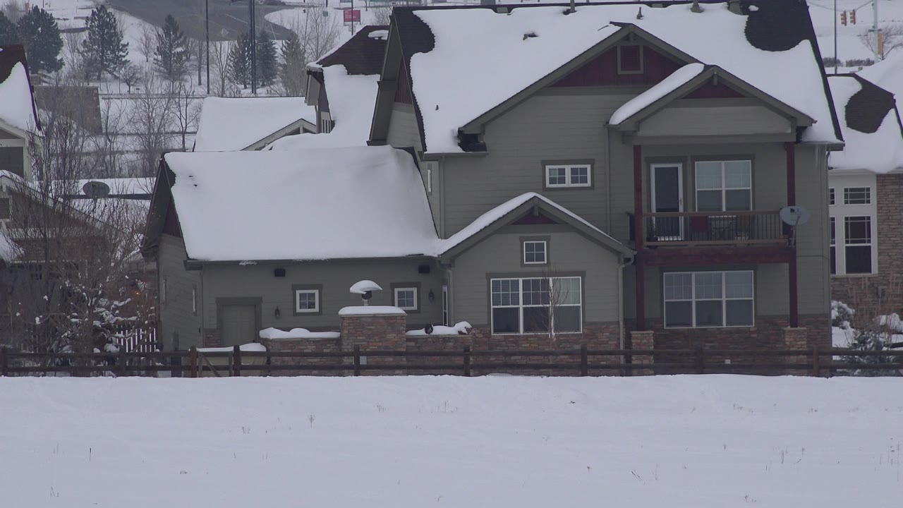 Large Arvada, Colorado house with heavy snow on the rooflines, a fence and stone posts in front, and no visible people in the snowfield.