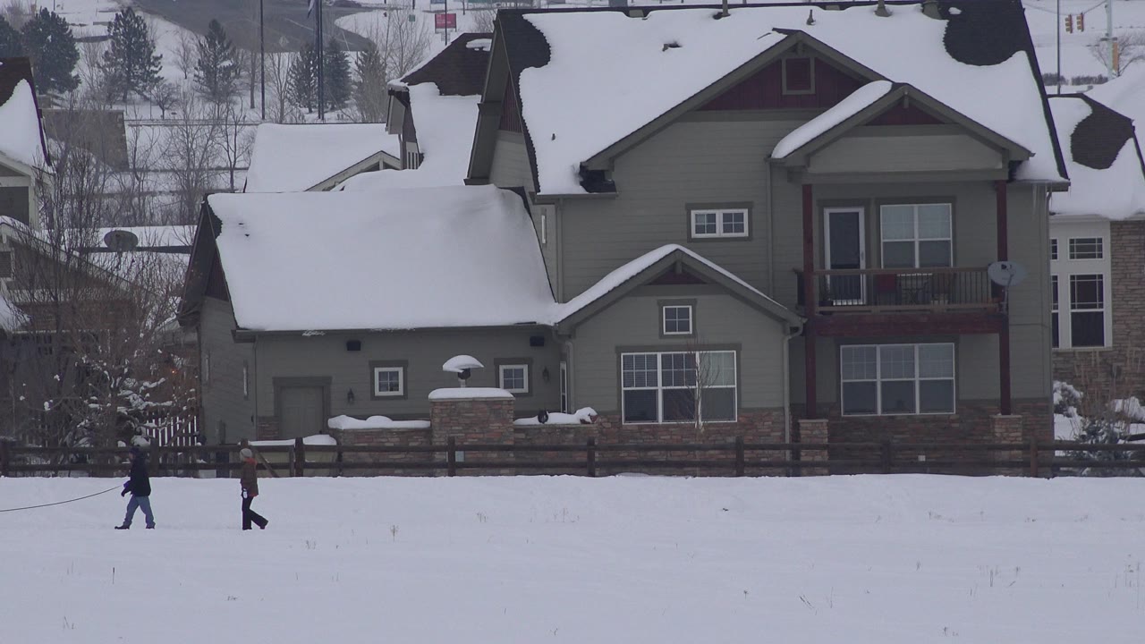 Two people walking across a snowy field in front of a house