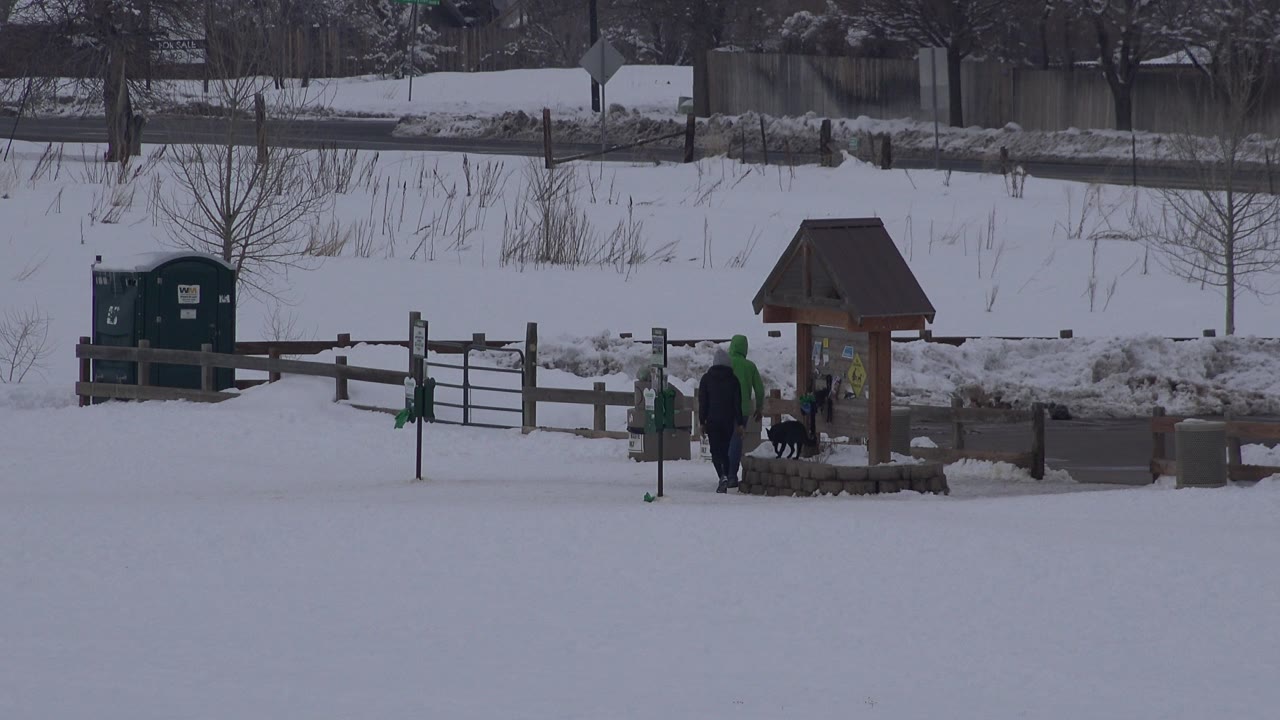 Adult, child, and dog stand beside the small roofed structure in snow.