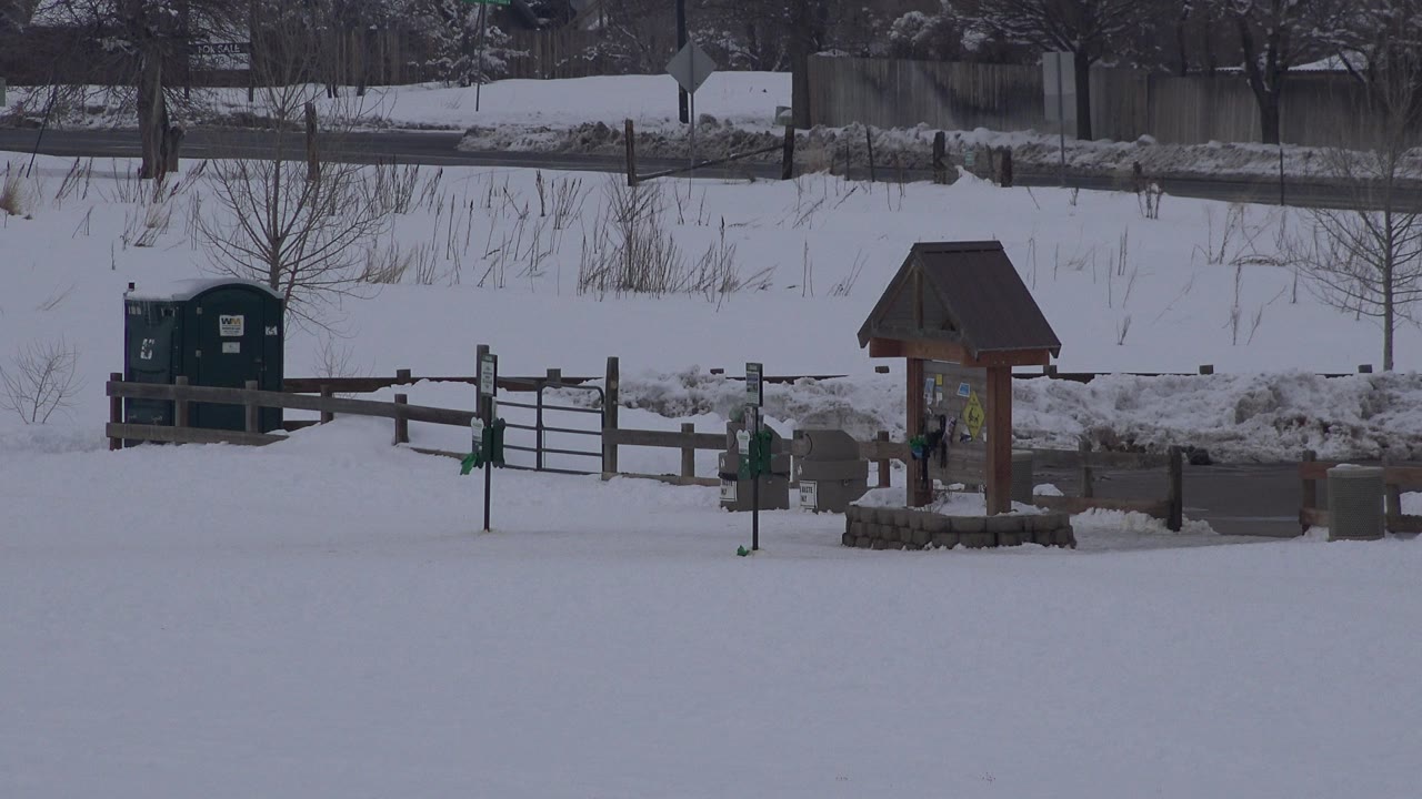Snow-covered farm area with fence, portable bathroom, and wooden sign kiosk.