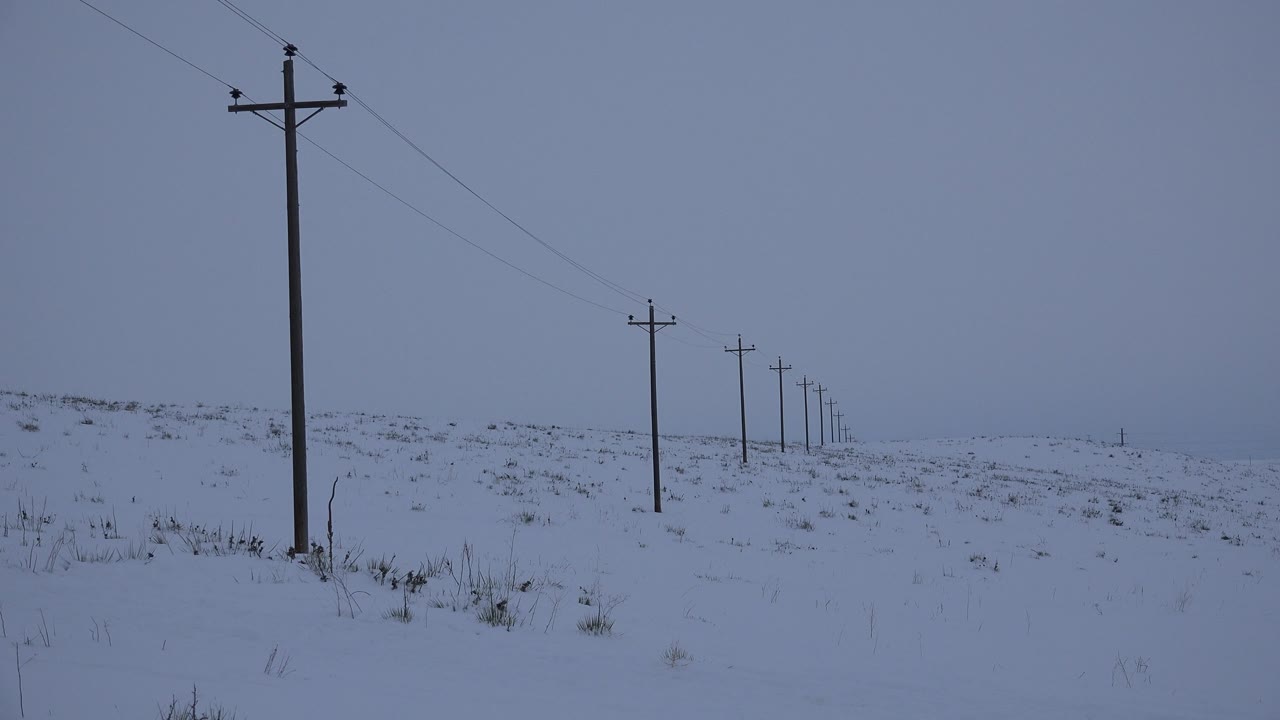 Arvada, Colorado winter frame with a dark wooden pole near the left foreground, wires slanting across the sky, distant poles, drifting snow cover, and no visible people.