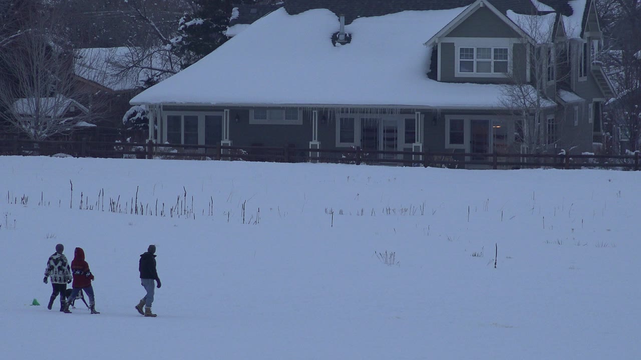 Bundled people walk across a snowy field near a house.