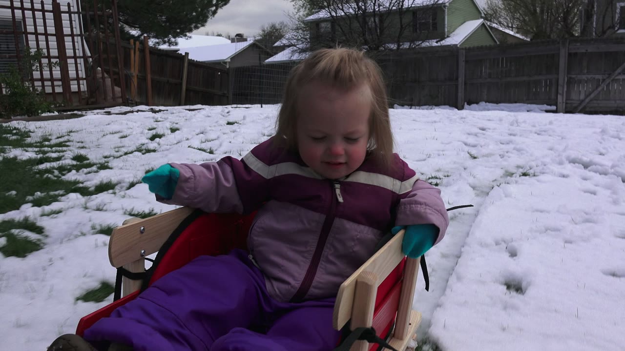 Toddler sitting in a red sled on a snowy lawn.