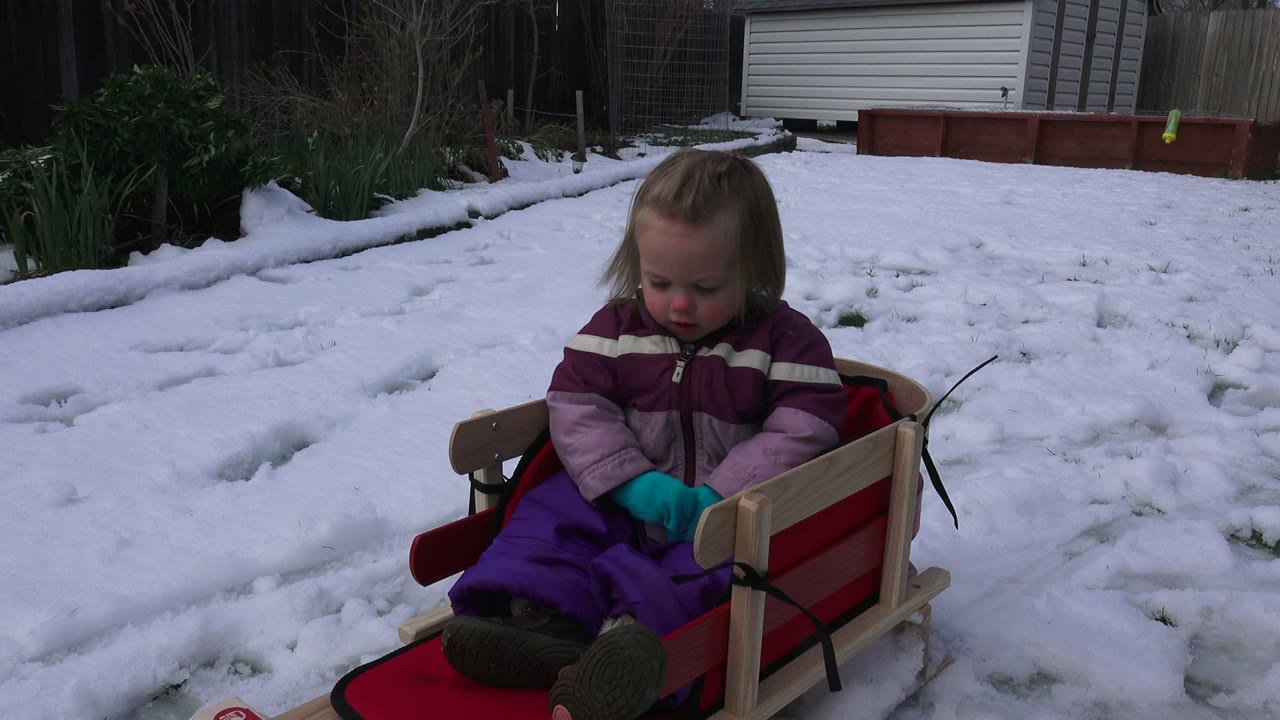 Young girl sitting in a red sled on snow.