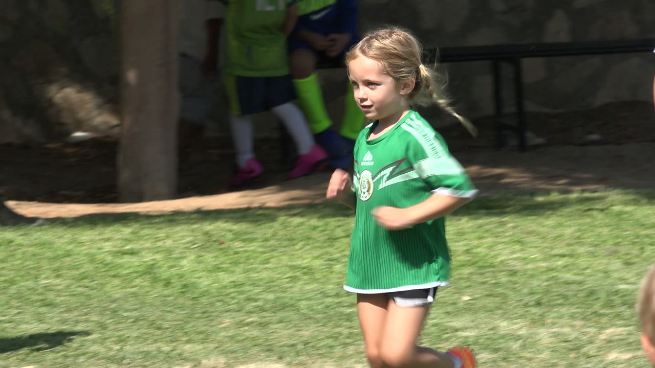 Blonde girl in a green soccer jersey running on grass.