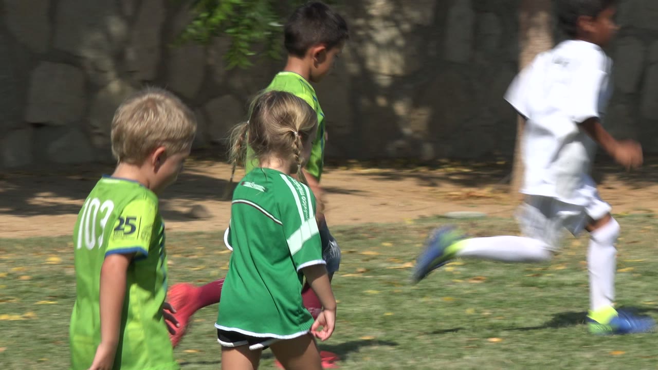 A child in a white soccer uniform runs across the field while children in green jerseys stand and walk nearby in San Jose del Cabo, Mexico.