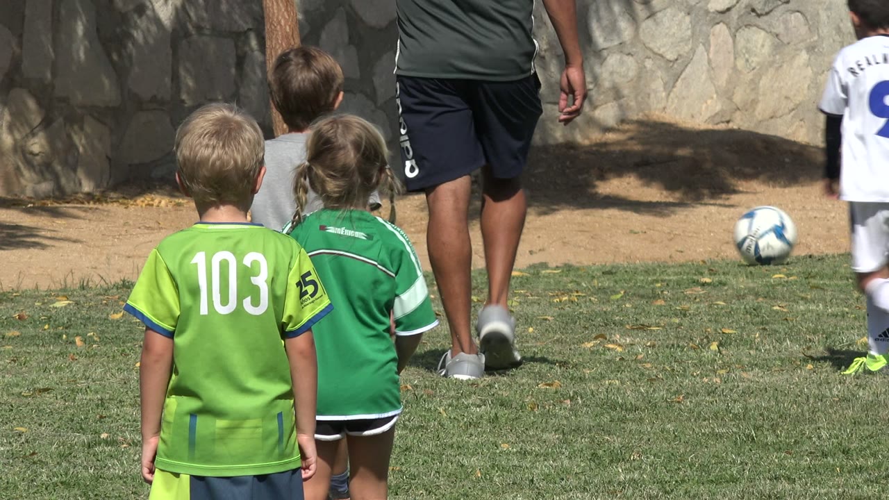 Children in green soccer uniforms walk on a grass field beside adults.