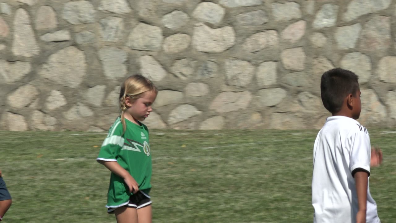 A blonde child in a green jersey walks through the midground in San Jose del Cabo, Mexico, with another child in a white jersey partly visible against the stone wall.