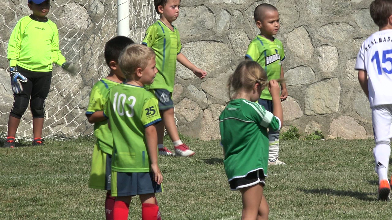 Children in green and white soccer uniforms stand beside the goal in San Jose del Cabo, Mexico, with jersey numbers and faces visible.