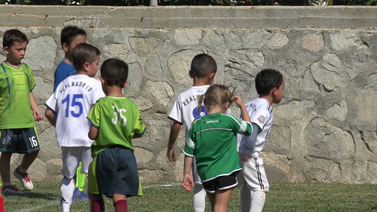 Kids in soccer kits gather near the wall during play.