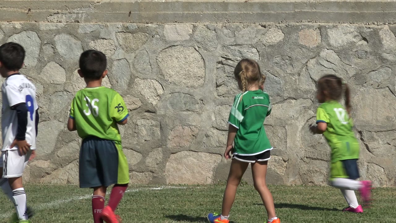 A girl in a green jersey stands near boys in white and green soccer uniforms on grass in San Jose Del Cabo, Mexico.
