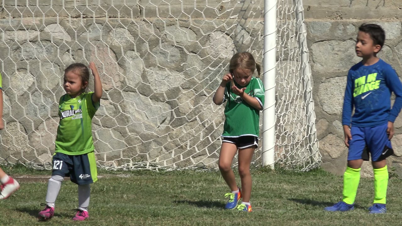 At the start of the clip, children in green and blue soccer uniforms stand near a white goal net on a grass field in San Jose Del Cabo, Mexico.