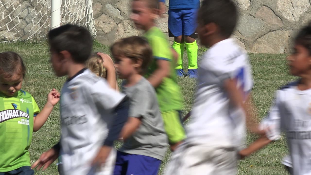 Children in soccer uniforms running across a grass field.