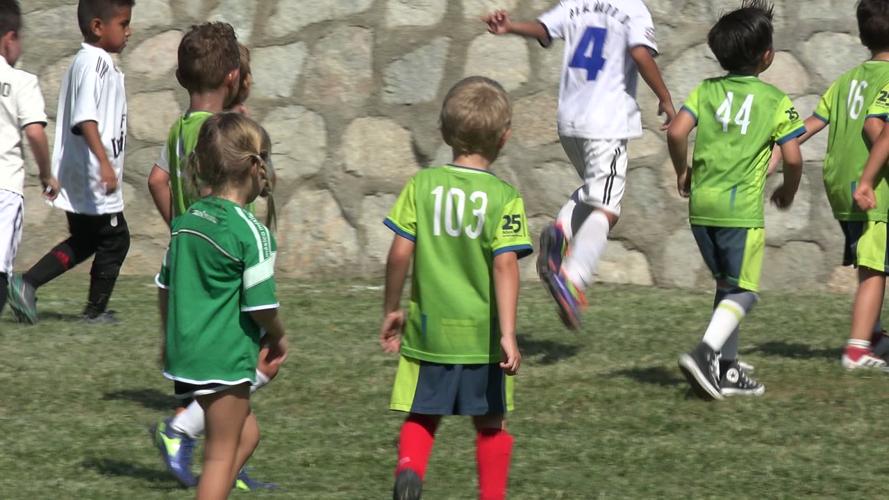 Several children in green and white uniforms move across the grass in San Jose del Cabo, Mexico, while one green-shirted child stands closer to the camera.