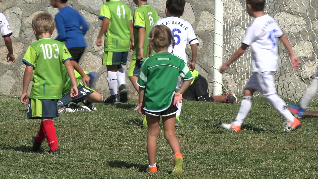 A group of children in green and white kits crowd the goalmouth in San Jose del Cabo, Mexico, while one child appears low to the ground near the net.