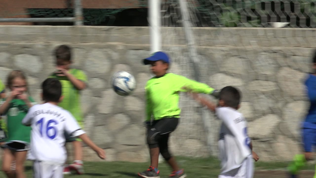 A soccer ball is in motion between children in green and white uniforms on a grassy field in San Jose del Cabo, Mexico.