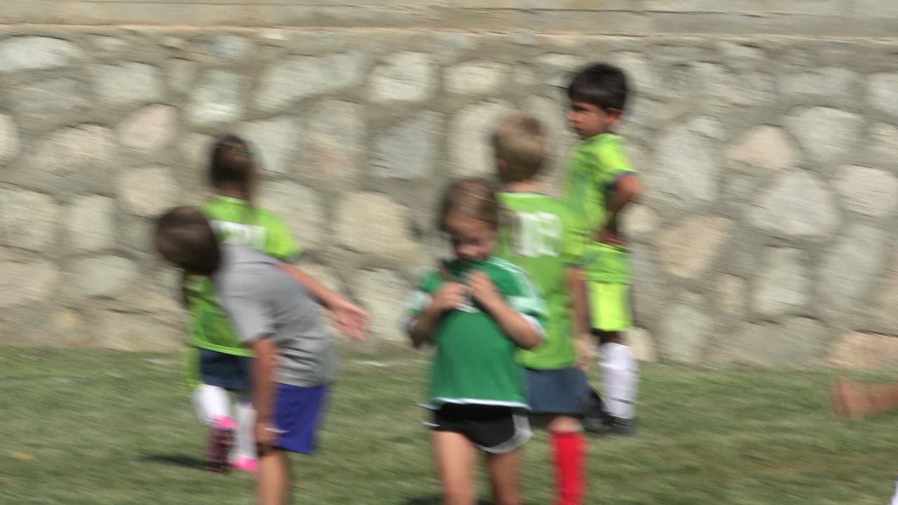 Close view of children in green and gray soccer clothes near a stone wall.